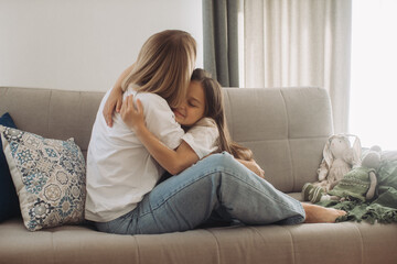 Obraz premium Smiling mommy sitting on sofa with little daughter, showing love. Hilarious mother nanny babysitter tickling small kid girl, having fun together on comfortable couch, enjoying priceless time at home.