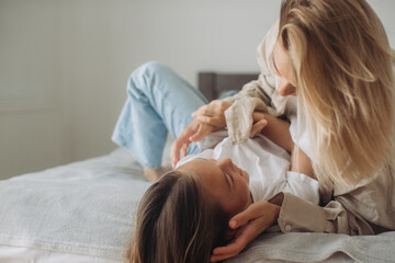 Happy mother and daughter having fun and playing together on the bed at home.