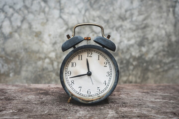 An old black alarm clock that was battered and rusted vintage retro style on the wooden table with background bare plaster or loft style.