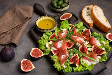 Italian appetizer prosciutto ham , blue cheese, figs, olives and ciabatta on a wooden board, dark rustic background. Side view, selective focus