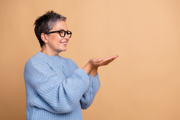 Photo portrait of lovely retired female palms hold empty space dressed stylish blue knitted outfit isolated on beige color background