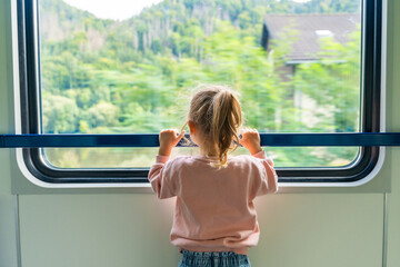 Beautiful little girl looking out train window outside, during moving. Traveling by railway in...