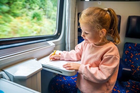Beautiful Little girl draws with pencils on white paper while traveling by railway, Europe