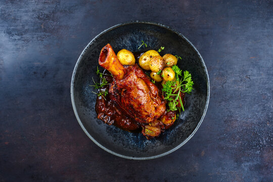 Traditionelle geschmorte Lammhaxe in Rotwein Sauce mit Mini Bratkartoffel und Kr&auml;uter serviert als Draufsicht in einer Nordic Design Schale mit Textfreiraum