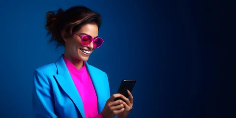 Foto op Plexiglas Colorful studio portrait of a beautiful young businesswoman, using a smartphone and smiling, blue and purple or pink. Copy space © Mihai Zaharia