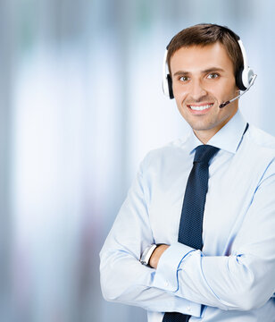 Call center help line service. Portrait photo of customer support phone sales male operator in headset, on blurred office background. Smiling confident business man. Caller worker