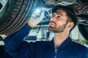 Car repair service. Handsome young technician checking car condition in garage, Automotive mechanic pointing flashlight following at maintenance checklist document.