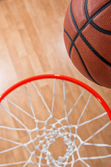 A close-up view looking down at an orange basketball almost going through the rim and a white nylon...