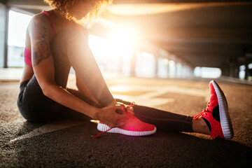 Young fit woman tying her shoelaces before jogging under a bridge in the city