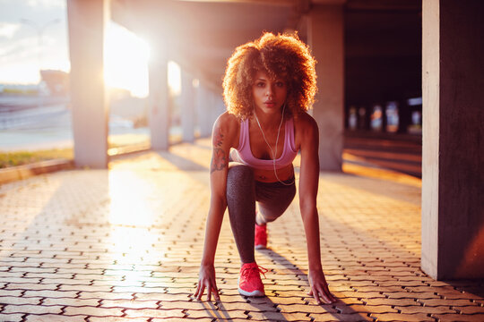 Young fit woman doing a crouch start before running under a bridge in the city