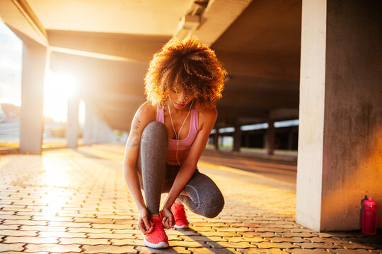 Young fit woman tying her shoelaces before jogging under a bridge in the city