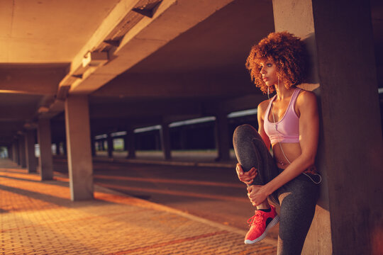Young fit woman stretching before jogging under a bridge in the city