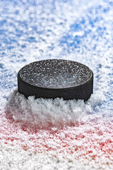 A black ice hockey puck plowing through snow and stopping on the edge of the Goal Line of the goal...