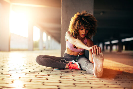 Young fit woman stretching before jogging under a bridge in the city