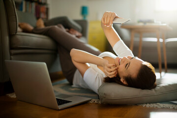 Young woman using her smartphone on the floor of her living room at home