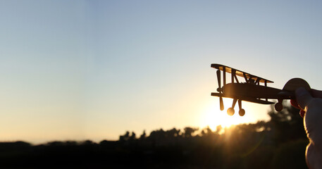 close up photo of man's hand holding toy airplane against sunset sky