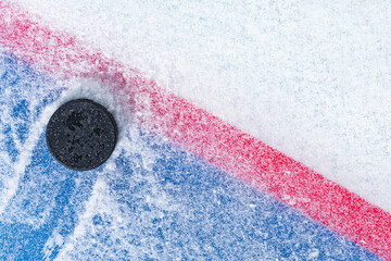 Looking down on a black ice hockey puck plowing through snow and stopping on the edge of the Goal Line of the goal crease.  - obrazy, fototapety, plakaty