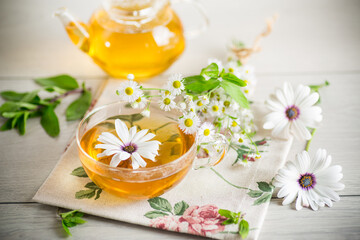 Chamomile flower tea in a glass cup and teapot, on a wooden table.
