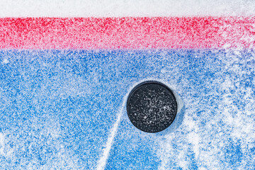 Looking down on a black ice hockey puck plowing through snow and stopping on the edge of the Goal...