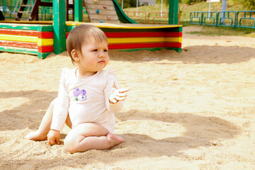 funny baby sits in the sand on the playground