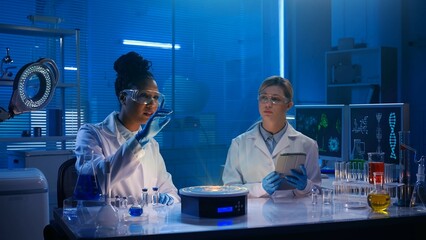 Medium-sized photo capturing two female scientists wearing glasses and lab coats sitting in a laboratory, researching a hologram, your graphics.