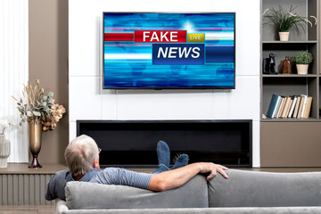Elderly man watching Fake News on TV sitting on the couch at home