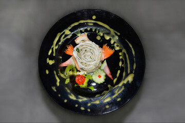 Olivier salad with mayonnaise is shaped into a cake and decorated with beautifully chopped vegetables and on a plate with a decorative pattern of spices and sauce on a gray background, flat lay