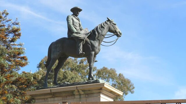 Kimberley, South Africa - September 2023: Side view looking up at Cecil John Rhodes statue. Tree branches move behind