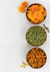 Assorted dried fruits: golden raisins, dried apricots and pumpkin seeds on a white background. Copy space.
