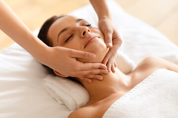 Fototapeta na wymiar Woman enjoying face building massage lying with eyes closed indoor