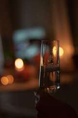 Close up shot of glass of champagne held by a hand indoors. Lit candles in the background.