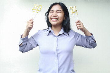 cheerful asian young woman holding candles number 2024 to celebrate new years eve party wearing grey shirt