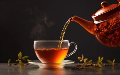 Foto op Plexiglas Pouring fresh and hot Rooibos tea from the teapot to a glass cup, dark background © Aliaksandra