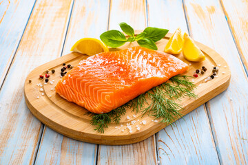 Fresh raw salmon steak with salt and fresh vegetables on wooden background
