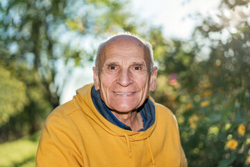 Naklejka na ściany i meble Wrinkled face of healthy happy smiling elderly male person in garden outdoors on green nature background and sunlight