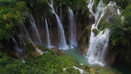 Waterfalls in green mountain forest landscape with streams of water. Cascades flow among lush greenery in spring or summer.