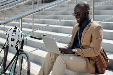 Young African American male solopreneur or freelancer typing on laptop keyboard while sitting on...