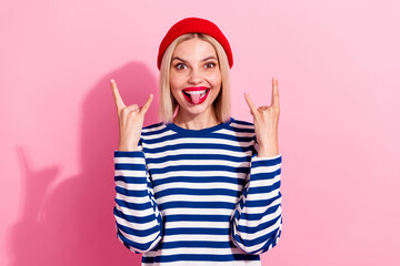 Photo of young funny girl blonde wearing beanie red hat joking showing fingers brutal punk fan tongue out isolated on pink color background