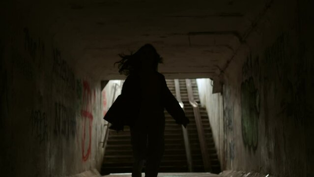 A girl runs in an underground tunnel. A dark and dirty tunnel without light. Dramatic shot, scary atmosphere. A neglected underpass through which a woman runs