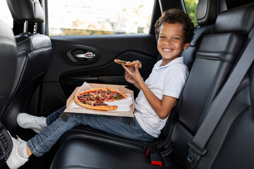 Boy eating pizza while sitting in a car back seat