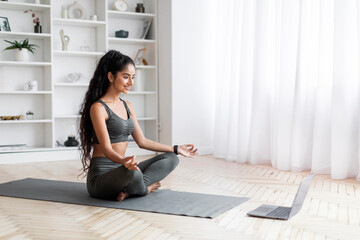 Positive pretty young sporty lady meditating at home, using laptop