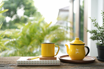 Yellow cup and tea pot and on wooden tray and plant pot on wooden table