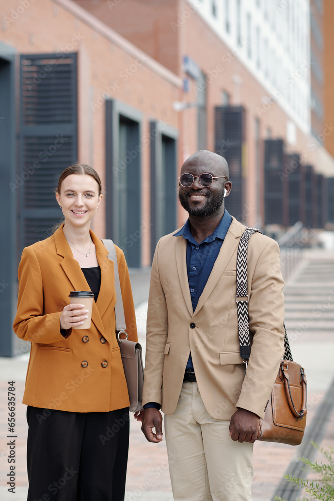 Poster Young intercultural white collar workers in formalwear standing against part of modern architecture in urban environment and looking at you