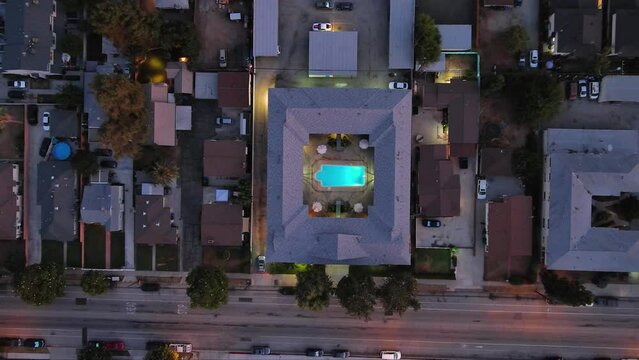 overhead descending aerial footage of a pool in the center of an apartment buildings surrounded by houses, condominiums and trees with cars driving on the street at sunset in Monrovia California