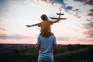 Dad and son playing together outdoors with yellow plane. Father and son launch a toy airplane at...