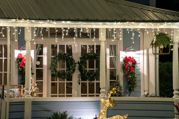 House front yard with big porch brightly illuminated with christmas decorations. Outside decor of...