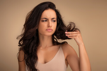 Stressed young brunette woman looking at unhealthy split ends hair