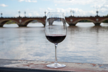 Tasting of Bordeaux blended red wine with wine city Bordeaux on background, left bank of Gironde Estuary, France. Glass of red French wine.