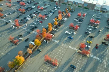 Fotobehang Top view of many cars parked on a parking lot in front of a strip mall plaza. Concept of consumerism and market economy © bilanol