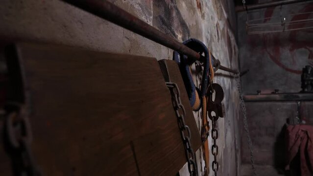 Close-up of an old rusty chain with handcuffs hanging on the gray dirty wall of the prison. Various scary tools in the torture room. The room of horrors. An old prison room.